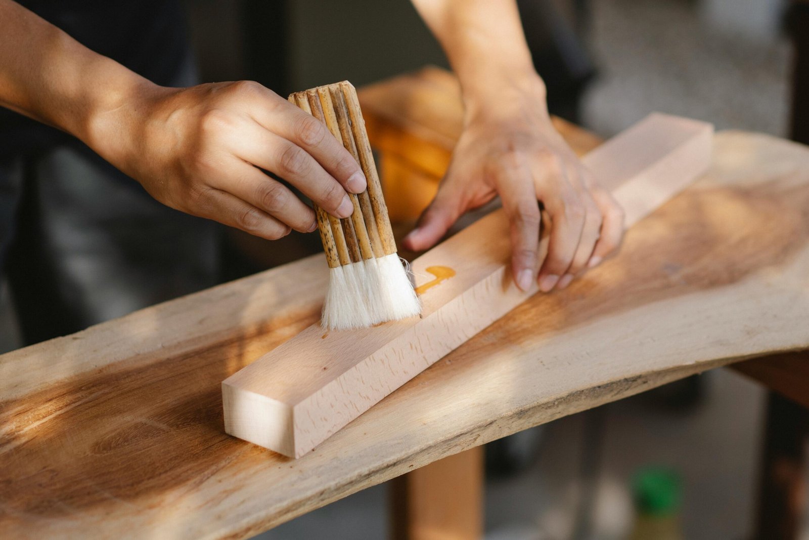 A craftsman applies oil to a wooden plank using a brush, showcasing skilled carpentry techniques.
